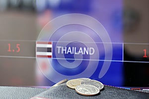 Pile of Thai baht coins on THB on black wallet with black floor and digital board of currency exchange money background.