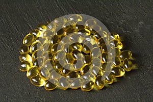 Pile of transparent capsules of golden yellow color lies on black modern background. Oil filled capsules vitamin A, vitamin D3,