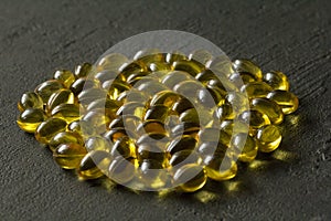 Pile of transparent capsules of golden yellow color lies on black modern background. Oil filled capsules vitamin A, vitamin D3,