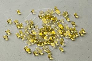 Pile of transparent capsules of golden yellow color lies on light gray modern background. Oil filled capsules vitamin A, vitamin