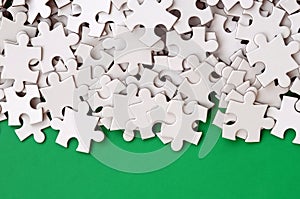 A pile of uncombed elements of a white jigsaw puzzle lies on the background of a green surface. Texture photo with copy space for