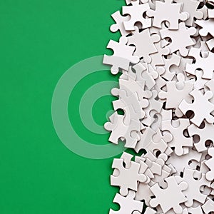 A pile of uncombed elements of a white jigsaw puzzle lies on the background of a green surface. Texture photo with copy space for