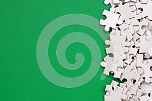 A pile of uncombed elements of a white jigsaw puzzle lies on the background of a green surface. Texture photo with copy space for