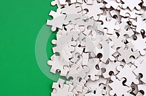 A pile of uncombed elements of a white jigsaw puzzle lies on the background of a green surface. Texture photo with copy space for