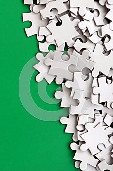 A pile of uncombed elements of a white jigsaw puzzle lies on the background of a green surface. Texture photo with copy space for