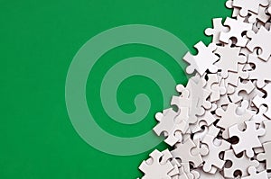 A pile of uncombed elements of a white jigsaw puzzle lies on the background of a green surface. Texture photo with copy space for