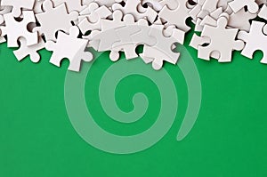 A pile of uncombed elements of a white jigsaw puzzle lies on the background of a green surface. Texture photo with copy space for