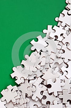 A pile of uncombed elements of a white jigsaw puzzle lies on the background of a green surface. Texture photo with copy space for