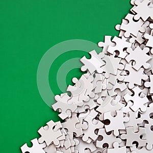 A pile of uncombed elements of a white jigsaw puzzle lies on the background of a green surface. Texture photo with copy space for