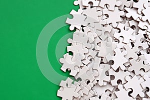 A pile of uncombed elements of a white jigsaw puzzle lies on the background of a green surface. Texture photo with copy space for