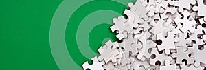 A pile of uncombed elements of a white jigsaw puzzle lies on the background of a green surface. Texture photo with copy space for