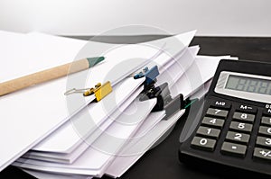 A pile of unfinished documents, a calculator and a pen on an office desk, a desk made of business paper. Close-up.