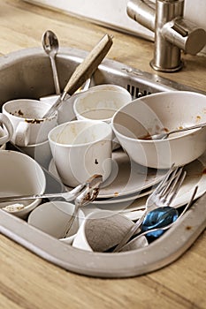 Pile of unwashed, dirty dishes in the sink. Mess in the kitchen. Dirty kitchenware, plates and mugs. Chaos at home