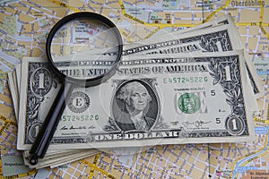 Pile of US dollar cash and a magnifying glass. European map covered with money, America with one dollar banknotes.