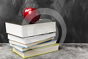 Pile of various books and red apple on dark background. Copy spa
