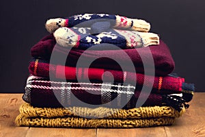 Pile of warm and cosy winter and autumn clothes on wooden background Sweaters cardigans scarf mittens Toned