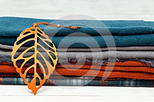 Pile of warm woolen scarf lying on wooden table and decorated autumn leaves
