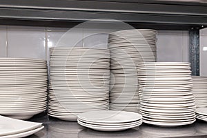 A pile of white clean ceramic porcelain plates on a metal rack in the back of the restaurant. Concept of preparation for banquet,