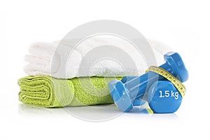 Pile of white and green towels with two blue vinyl coated dumbbells wrapped with yellow measuring tape. Healthy leaving and fitnes