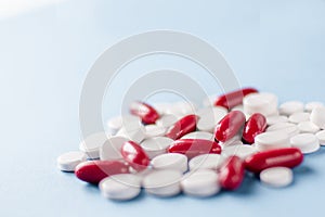 Pile of white pills and red capsules on blue medical background