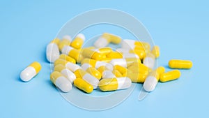 Pile of white and yellow pills on blue background. Concept of medical treatment with medicine, vitamins or supplements