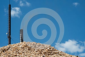 A pile of wood chips with a blue sky and a chimney in the background