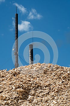A pile of wood chips with a blue sky and a chimney in the background
