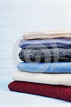 Pile of wool sweaters and knitted winter clothes on blue wooden background. Copy space for text.