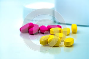 Pile of yellow and pink tablets pills on blurred background of plastic pills bottle with copy space. Ibuprofen for relief pain.