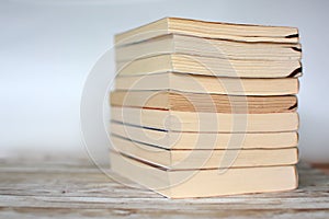 Pile of yellowed old used paperback books on wood desk and light blue background