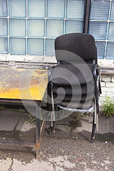 Piled old dirty dusty office chairs and a rusty weathered yellow metallic table standing outside