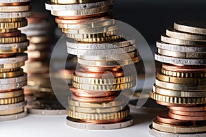 Piled up coins, Euros in different sizes leaning to the right on white surface and dark background