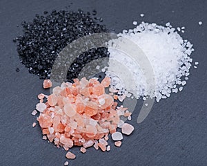 Piles of Hawaiian Black Lava Sea Salt, Coarse White Sea Salt and Himalayan Pink Salt on dark