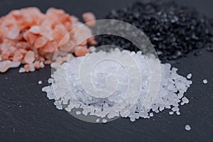 Piles of Hawaiian Black Lava Sea Salt, Coarse White Sea Salt and Himalayan Pink Salt on dark