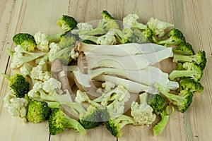 Piles of King Oyster Mushrooms (Pleurotus Eryngii) over bunch of fresh green sliced broccoli on the wooden chopping block