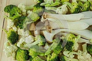 Piles of King Oyster Mushrooms (Pleurotus Eryngii) over bunch of fresh green sliced broccoli on the wooden chopping block