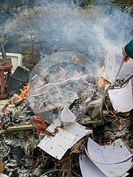 Piles of paper archives and documents burn outdoors in a controlled fire, destroying old files for security or disposal.