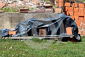 Piles of red building blocks and bricks mixed with construction material and other junk next to old concrete foundation