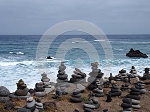 Piles of stacked stone towers on a beach with surf waves and blue sky