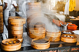 Piles of stacking bamboo steamers are steaming for dim sum in front of the restaurant with blur chefs in background in Taipei