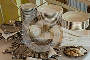 Piles of white clean plates, table knives, forks, spoons, napkins. Preparing for guest service in the restaurant