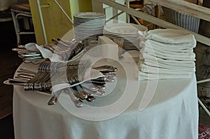 Piles of white clean plates, table knives, forks, spoons, napkins. Preparing for guest service in the restaurant