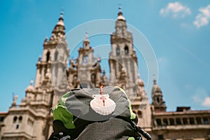 Pilgrim`s backpack with famous pilgrims` mascot and sign seashell with Cross of Saint James at  on the Obradeiro square plaza