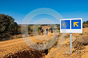 Pilgrims with backpack walk along Saint James way, also known as Camino de Santiago, on a sunny day in the countryside, with arrow