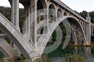 Pilings and arches of the Rogue River bridge in Gold Beach, Oregon at sunset reflected in water