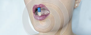 Pill between beautifully maked up female lips. A woman holds a pill between her lips. Analgesic, antipyretic medicine for the