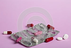 Pill blister pack and some colorful capsules on a pink background