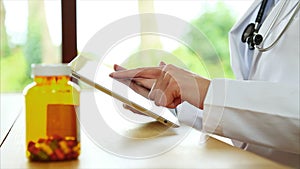 Pill bottle on desk with doctor using digital tablet in medical clinic