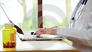 Pill bottle with female doctor's hands typing on laptop