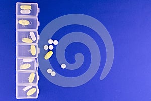 Pill box with days of the week and different pills on a blue background. Copy space.